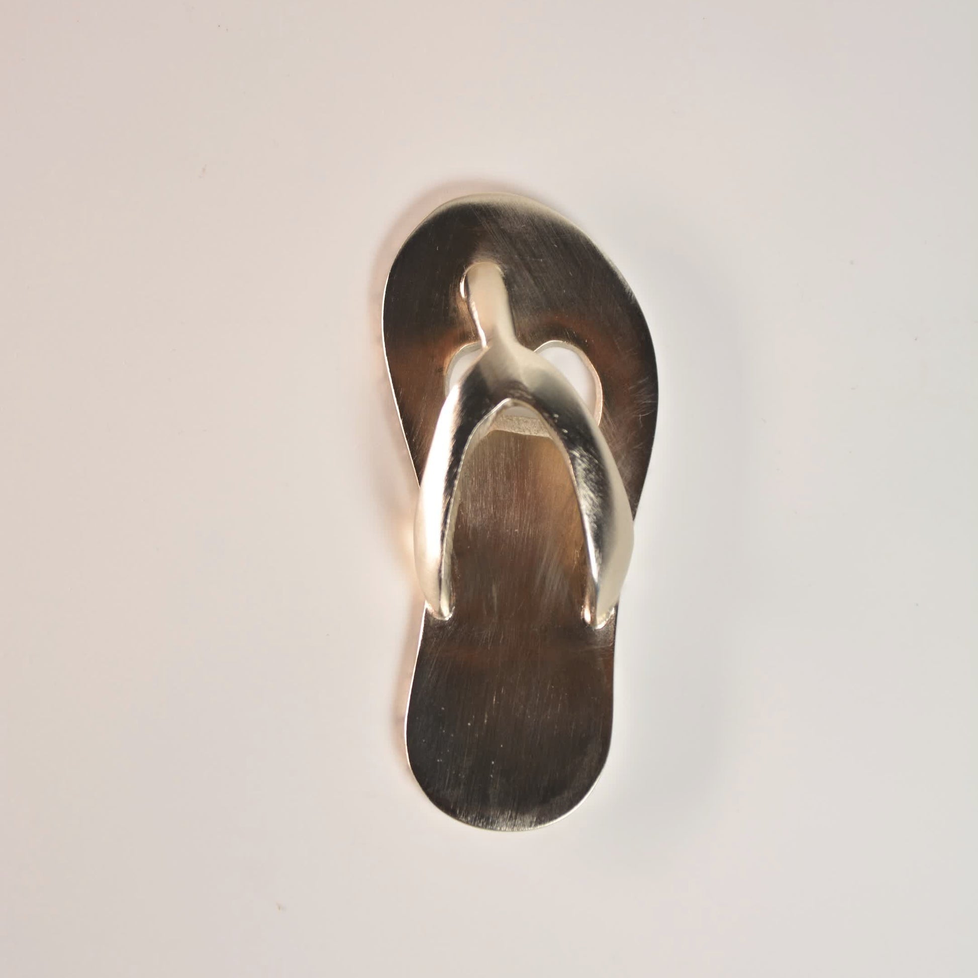 metal flip flop bottle opener on a light gray background